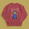 A holiday sweatshirt featuring a cute Grim Reaper holding a scythe, wearing a Santa hat. Above the character is the text "Grave Tidings We Bring," surrounded by festive snowflakes and holiday-themed designs. The combination of spooky and festive elements adds a humorous twist to traditional holiday attire.